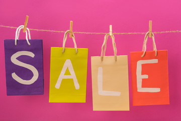 colorful sale signs on shopping bags hanging on rope isolated on pink, offer sale tags