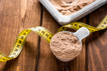 nutrition for workout with protein cocktail powder, measure tape on wooden background close up