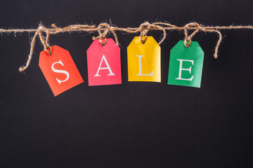 Close-up view of colorful sale sign on tags hanging on rope isolated on black, Offer sale tags
