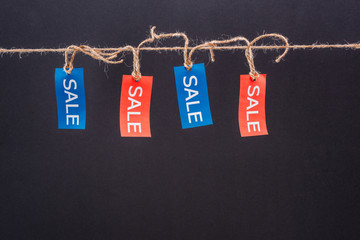 Close-up view of red and blue sale tags hanging on rope isolated on black, Offer sale tags