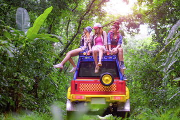 woman in group are enjoy traveling by sitting on the rack-roof of the convertible car off-road in jungle