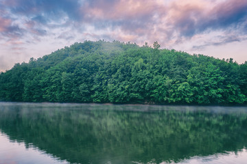 Nature mirror world wallpaper, soft pink sunset over the river with green hill and cloudy sky. Recreation area reservoir Ruzin near Kosice, Slovakia