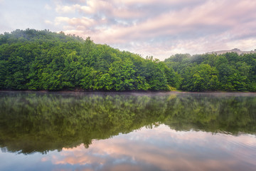 Obraz premium Beauty of nature wallpaper, pink sunset over green hill with reflection in the water. Recreation area reservoir Ruzin near Kosice, Slovakia