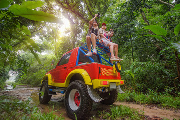 woman in group are enjoy traveling by sitting on the rack-roof of the convertible car off-road in jungle