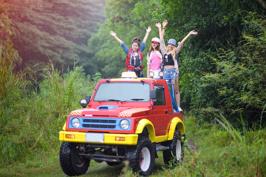 woman in group are enjoy traveling by standing on the rack-back of the convertible car off-road in jungle