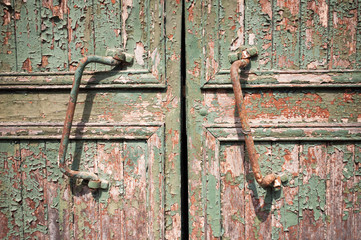 Close-up of two rusty door handles on an old and decrepit wooden barn door with peeling paint