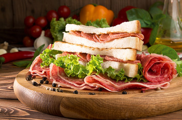 Sandwich with salami. Lettuce, cherry tomatoes, mustard, basil, garlic on wooden background.