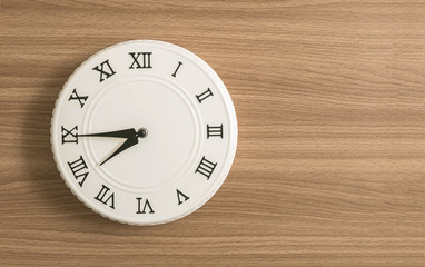 Closeup white clock for decorate show a quarter to eight o'clock or 7:45 a.m. on wood desk textured background with copy space