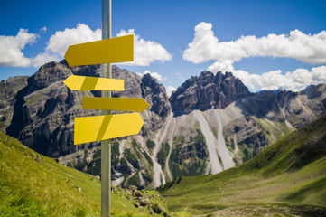 Blank hiking signs on a pole in front of a blurred landscape with mountains and blue sky