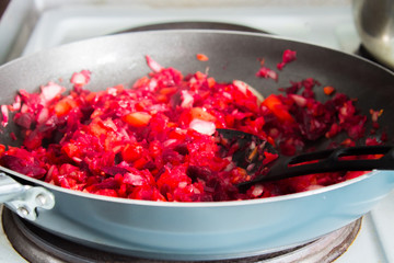 Carrots, beets and onion in a frying pan are roasted on the stove. Ingredients for borsch.