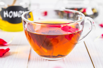 Floral black tea, honey can, petals on a white wooden table.