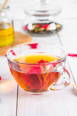 A cup of tea, in the background of a bank with a black herbal floral tea on a white wooden table.