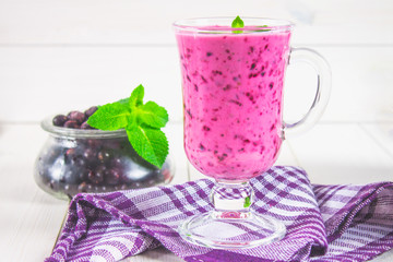 Smoothies of black currant in a glass with a handle on a white wooden table.