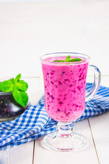 Smoothies of black currant in a glass with a handle on a white wooden table.