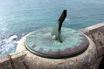 Antique sundial on a stone wall overlooking the sea - obrazy, fototapety, plakaty