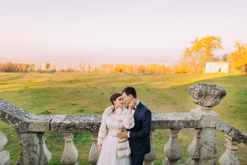 The bride is petting the face of the groom. The sensitive outdoor portrait.