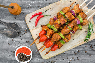 On a gray wooden surface on the board is a chicken barbecue grilled, with vegetables, spices, rosemary,  hand-made wooden pepper mill, large salt, paprika, chili, fresh bread, lime, top view