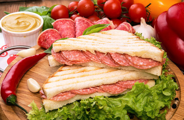 Sandwich with salami. Lettuce, cherry tomatoes, mustard, basil, garlic on wooden background.