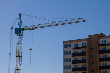 Fototapeta premium Building crane and building under construction against blue sky