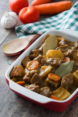 Beef meat stewed with potatoes, carrots and spices in ceramic pot on wooden table
