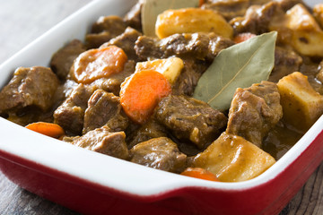 Beef meat stewed with potatoes, carrots and spices in ceramic pot on wooden table

