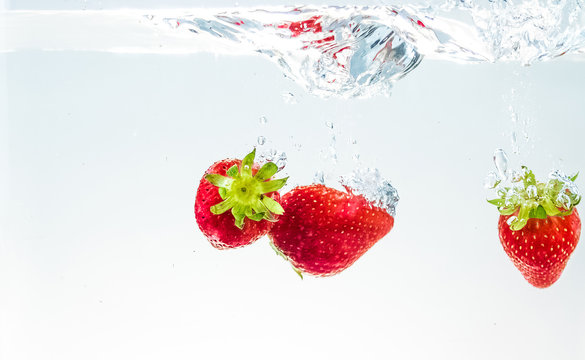 red fresh fruit strawberries falling into water with splash on white background, strawberry for health and diet, nutrition
