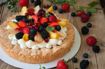 Homemade dacquoise cake with wipped cream cheese garnished with summer berries and peaches, close up.