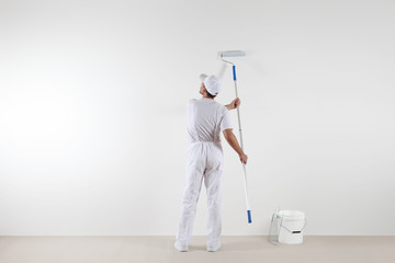 Rear view of painter man looking at blank wall, with paint stick roller and bucket, isolated on...
