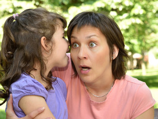 Fototapeta premium Daughter whispering secret into ears of surprised mother