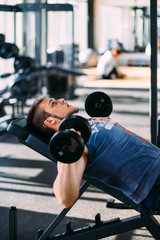 Fototapeta na wymiar Young handsome man working out with dumbbells in a fitness gym