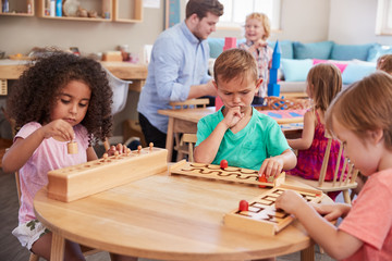 Teacher And Pupils Working At Tables In Montessori School