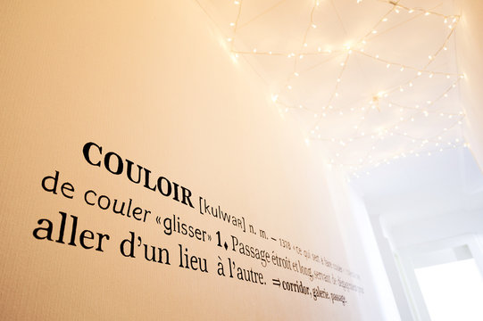  Long white corridor illuminated by a garland on the ceiling and decorated with a wall definition of the word corridor