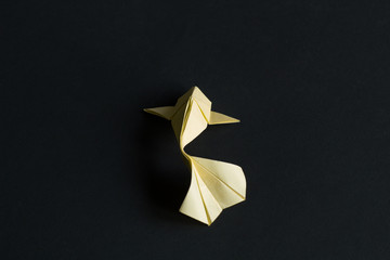 Handmade paper craft origami yellow koi carp fish on black background. Back view