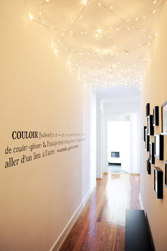  Long white corridor illuminated by a garland on the ceiling and decorated with a wall definition of the word corridor
