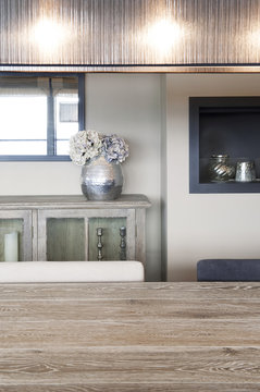 Salle &agrave; manger avec table en bois patin&eacute; clair, lampe design, buffet en bois et vase argent&eacute; avec hortensia