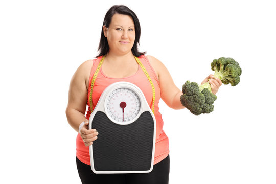 Overweight woman with weight scale and broccoli dumbbell