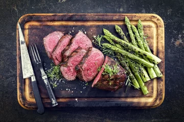 Gordijnen Barbecue Wagyu Point Steak with green Asparagus as close-up on burnt cutting board © HLPhoto