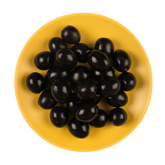 Black olives on a yellow plate isolated on white background.