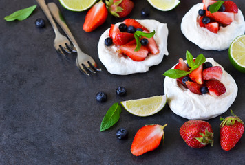 Dessert pavlov with strawberries and blueberries on a black background.