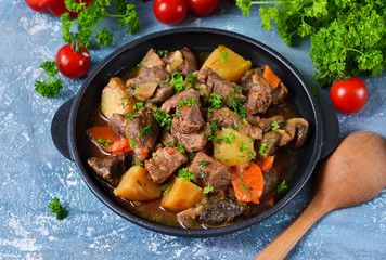Meat goulash with vegetables, potatoes and mushrooms on concrete, grunge background