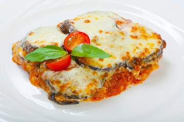 Baked eggplant with cheese, tomatoes and spices on a white plate. A dish of eggplant is on a wooden table.