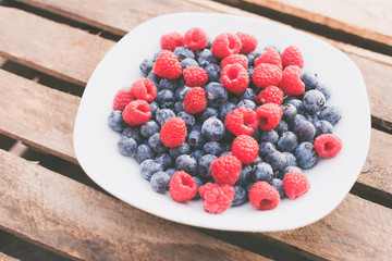 Himbeeren und Blaubeeren auf einem weißen Teller vor Holz Hintergrund
