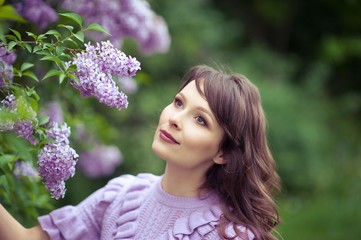 Fototapeta premium Young beautiful woman walks along the spring garden. A girl stands near the lilacs. Lilac. Flowers.