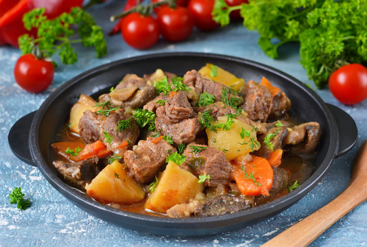 Meat goulash with vegetables, potatoes and mushrooms on concrete, grunge background