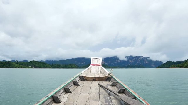 Longtail boat on Cheow Lan Lake, Khao Sok National Park, Thailand, with dramatic limestone cliffs, green hills, and a cloudy sky
