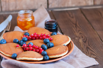 Stack of fluffy panckes with fresh berries, blueberry and orange jam served on a white plate. Healthy breakfast concept.
