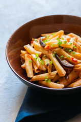 Penne pasta with egplants, tomatoes and green onions on a white stone background.