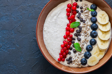 Super food smoothie bowl with oats, cootage cheese, milk, berries, sunflower seeds and banana on a black slate background.