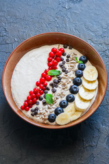 Super food smoothie bowl with oats, cootage cheese, milk, berries, sunflower seeds and banana on a black slate background.