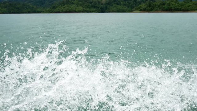 Dynamic water spray breaks the stillness of a lake, with a backdrop of tranquil water and a distant tree-lined shore